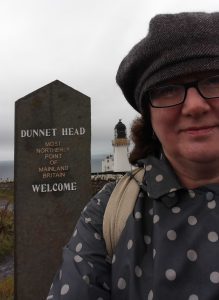 Photo of Debbie in hat and coat at northernmost point of mainland Britain