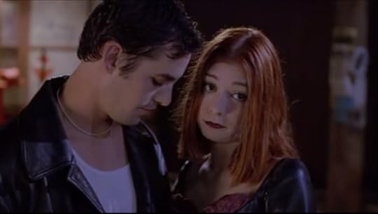 Willow and Xander are standing intimately close to each other. Xander is wearing a leather jacket a silver chain for some reason, and Willow has on dark makeup and a pleather corset get up.
