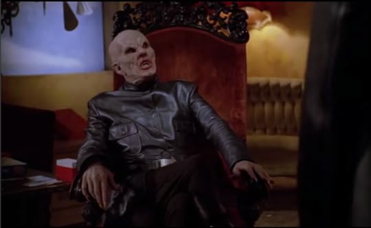 The leather clad, bald albino bat looking vampire from season one reclines sassily on a velvet throne.
