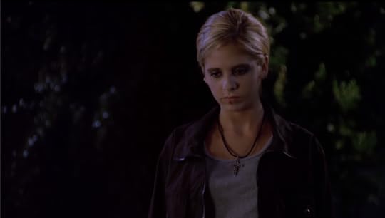 Buffy is wearing a grey shirt and a black leather jacket. Her hair is pulled back in a braid, she's got dark makeup on, and a big scar slashes across her lips.
