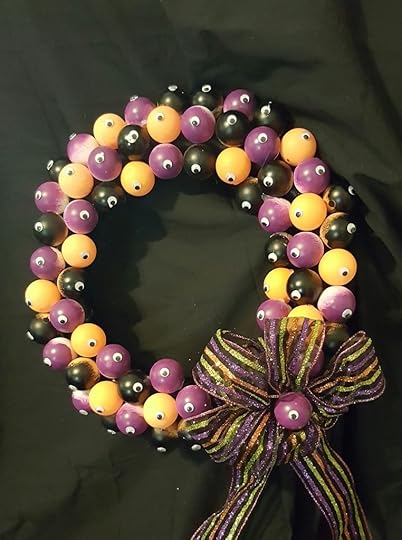It's wreath covered in ping pong balls painted purple, black, and orange. Well, the orange ones aren't painted, they started out orange. Each ping pong ball has a single googly eye on it, and there's a big stripy bow in Halloween colors, with another little eyeball in the center.
