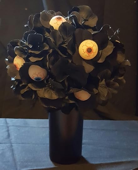 A black vase with black artificial flowers. Some of the flowers have eyeballs in them.