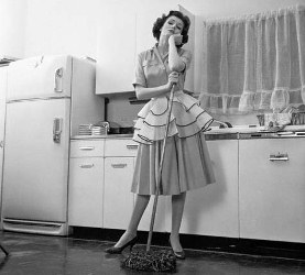 1954 --- 1950s Bored Woman Housewife Wearing Apron Leaning On Mop On Kitchen Floor --- Image by © Camerique/ClassicStock/Corbis