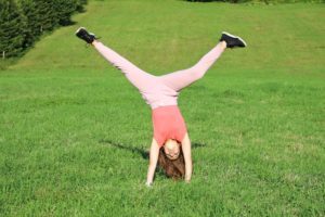 little girl doing catwheel on green field