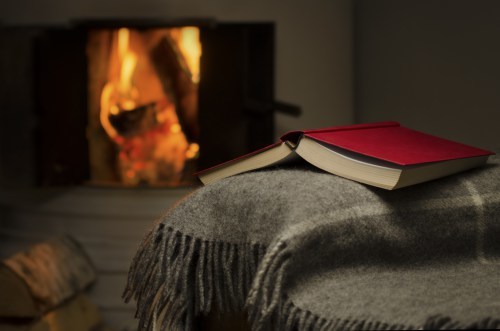 Peceful image of open book resting on a arm rest of a couch. Warm fireplace on background.