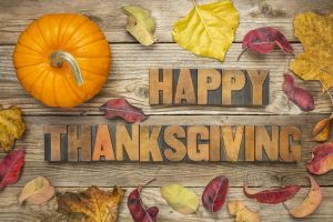 Happy Thanksgiving - text in vintage letterpress wood type blocks against rustic wood background with a pumpkin and dry leaves