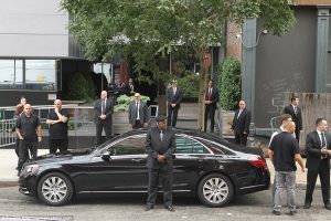 Black car parked outside hotel with many security guards around it