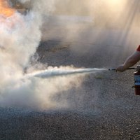A man crouches down using a fire extinguisher to control a blaze.