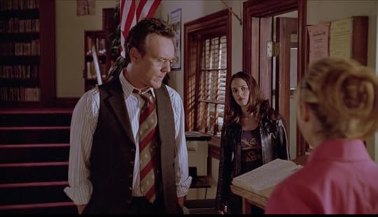 In the library, Giles stands with his back to Faith, who has just exited his office. Buffy stands in front of him (we see her from the back).