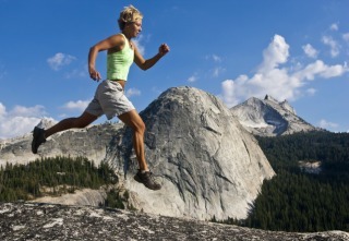 Female trail runner leaps an obstacle along a mountain top.