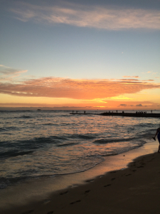 A beach, the waves and a orange and pink setting sun in Hawaii