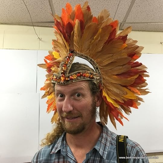 travel photographer Chad Case models feather headpiece at Ronnie of Ronnie & Coro Mas Camp costumes in Port of Spain, Trinidad