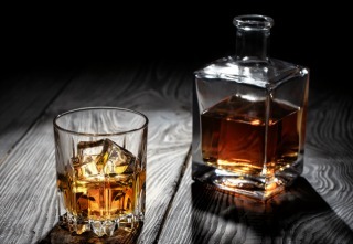 Backlit glass of whiskey with ice on wooden table