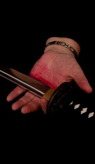 hand holding sword blade, fake blood on palm