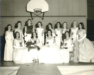 Women standing and sitting in a photograph, all dressed in pearl-white gowns, with smiling faces of resilience and determination.