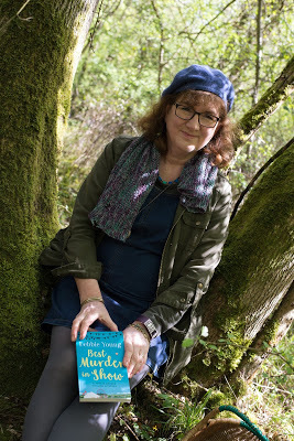 Debbie sitting in a bluebell wood with a copy of her book