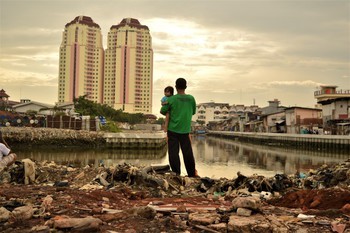 A father holds his daughter as he stands on a site from which local residents have recently been evicted to make way for new developments, close to luxury apartments in North Jakarta, Indonesia. Credit:  Tiara Audina / Oxfam Feb 2017