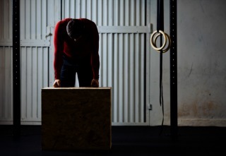 Tired sports man after box jumping exercise leaning on box. Dark picture.