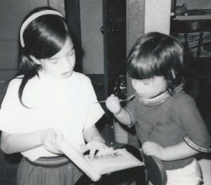 A girl of about 8 reads a book to a girl of about 3 or 4.