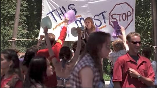 A woman with a bullhorn stands in front of a bedsheet sign that reads 