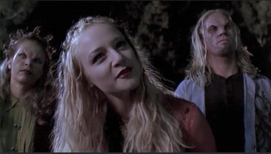 Three vampires. In the background, a red-headed one with her hair half-up in bantu knots and a goateed, surfer-haired dude. In the foreground, a girl with long blonde hair also half up in knots, but not the tall pointy one the other chick is sporting.