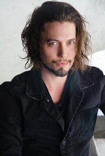 Dude has dark brown hair, brown eyes, and a dark goatee in this picture.