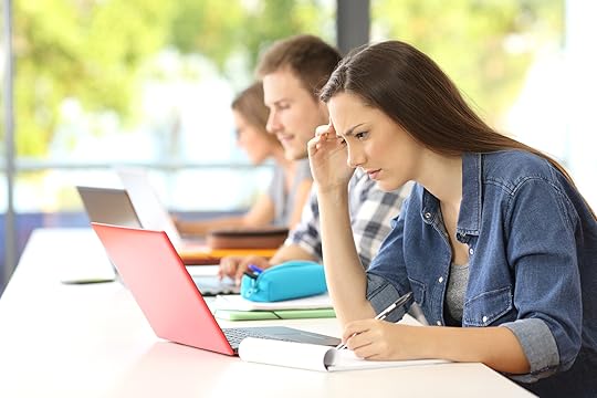 Side view of a concentrated student e-learning on line in a classroom with classmates in the background