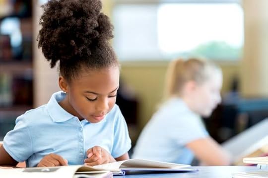 Cute African American schoolgirl reading a book in the library