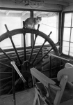 A cat sits atop the wheel in the pilothouse of an unknown steamer