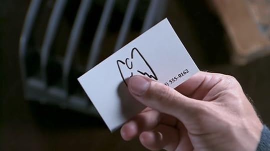 Angel holds a white business card with a stylized drawing that's basically a little oval with two wings.