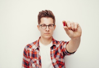 Young serious men in red shirt holding some pill hand. Isolated