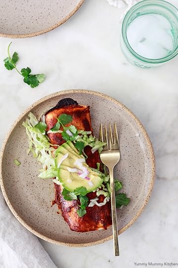One red vegan black bean enchilada on a rustic plate with shredded lettuce and avocado.
