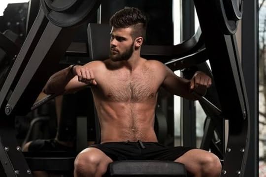 Photo of a shirtless, bearded man sitting at a chest press machine in a dark gym.