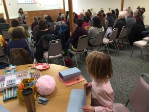 Blonde boy in back of crowd watching woman read