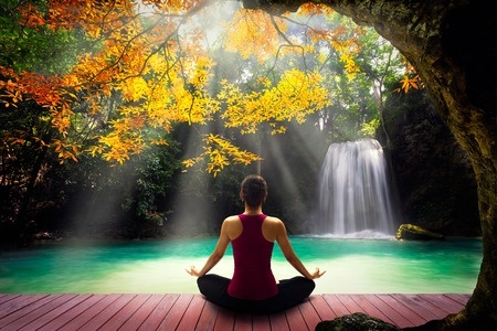41619177 - young woman in yoga pose sitting near watefall rear view