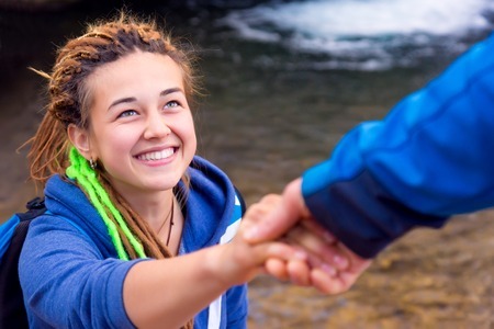 59668141 - two hikers young man and smiling woman holding hands helping each other walking mountain stream with waterfall vertical composition focus on girls face