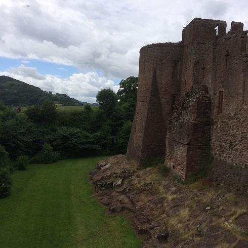 An image of a castle on the right, and on the left, green hills. Above, cloudy sky.