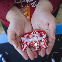 A pair of hands hold three circuit board badges for soldering.