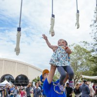 A young girl being held up by her father reaches to grab a dangling hand and give a high five.