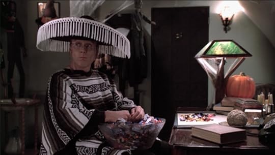 Giles is still in his stereotypical costume, sitting in his apartment at his desk with the trick-or-treat candy bowl in his lap, a mouth full of candy, and a pile of empty wrappers on the desk in front of him.