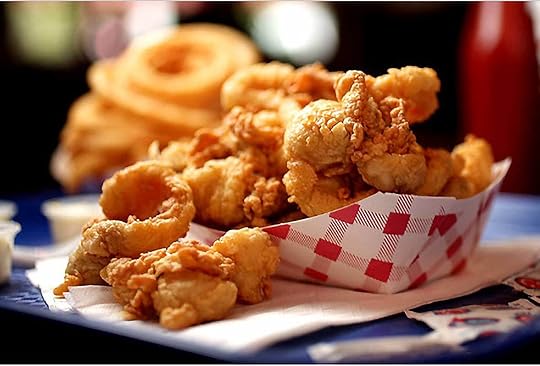 A red and white paper container of whole-belly fried clams, behind is onion rings and condiments