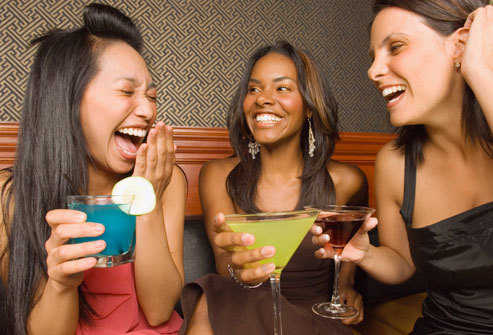 Three women holding drinks and laughing in bar