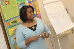 Teacher standing with pen in hand in front of a board with calendar words and easel