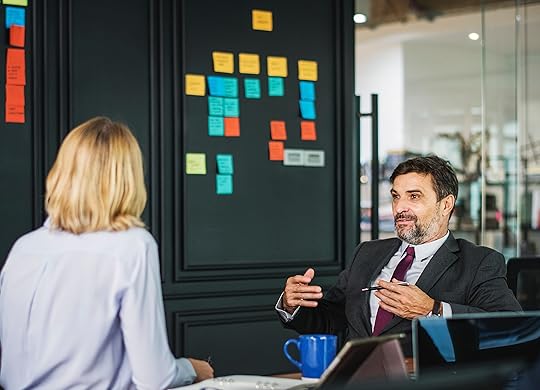 Man and woman sitting at a desk discussing work with sticky notes in background.