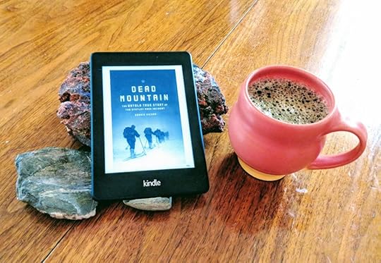 My Kindle Paperwhite propped up on some rocks on my dining room table, with a mug of coffee nearby.