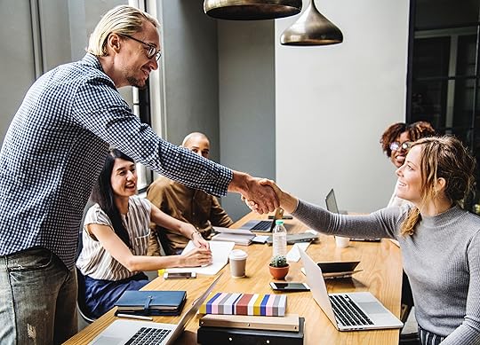 Man shaking hands with a team member across a conference room table in front of a group.