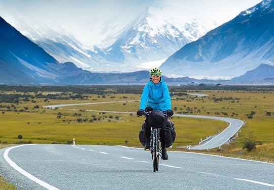 Cyclists winds along a road with snowy mountains to her back in New Zealand