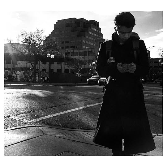 A young man reads his phone on a street corner. Shot by Jay Sennett