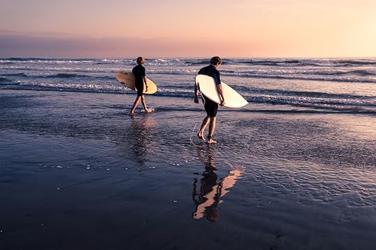 Surfers in black diving suits walking toward the water