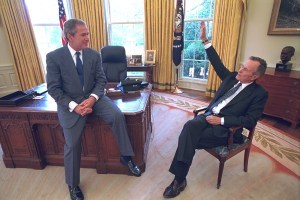 President George W. Bush sits on the edge of his desk Wednesday May 2, 2001, and talks with his father, former President George H.W. Bush who dropped by the Oval Office